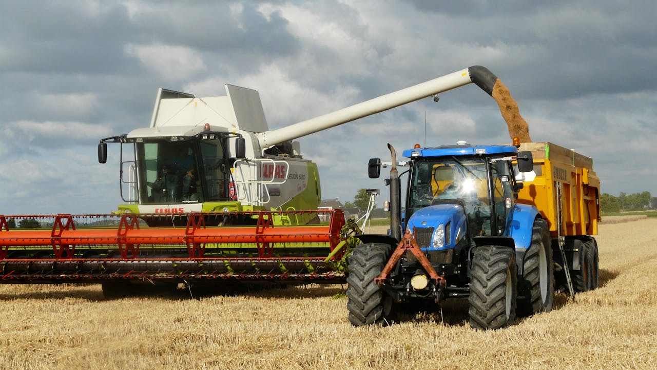 why-choose-us-02 A modern combine harvester and tractor working together to harvest wheat in a sunny outdoor field.