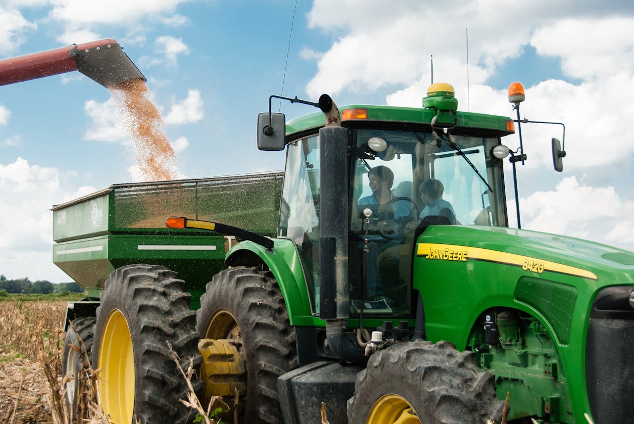 about-05 Green tractor harvesting crops in a sunny rural field, showcasing modern agriculture.